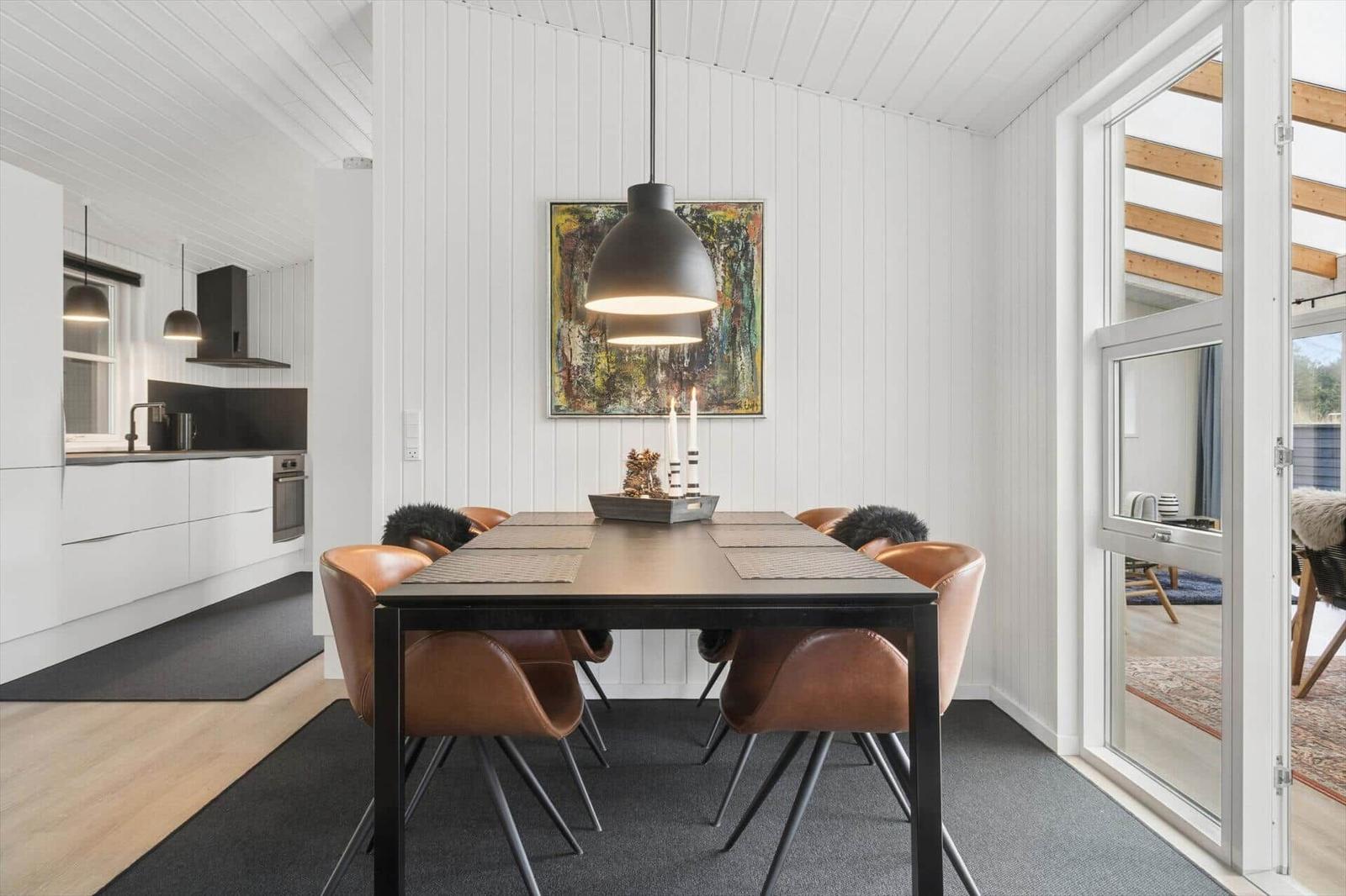 Essbereich mit Holztisch, Ledersitzen und Wandbild. Küche im Hintergrund. Durchgang zu Wohnbereich.