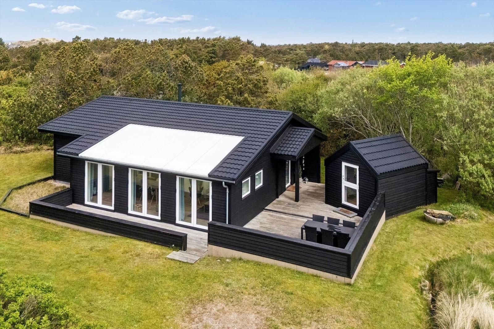 Moderne schwarze Villa mit Terrasse und Garten. Umgeben von Wald und Grünflächen.