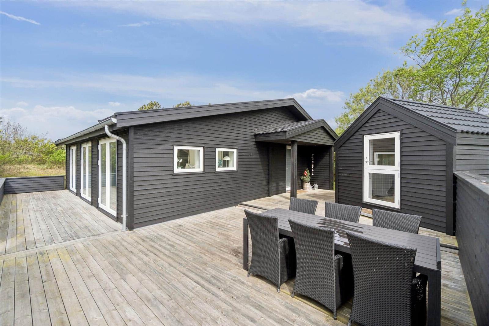 Schwarze Holzhütte mit Terrasse und Sitzgruppe im Freien.