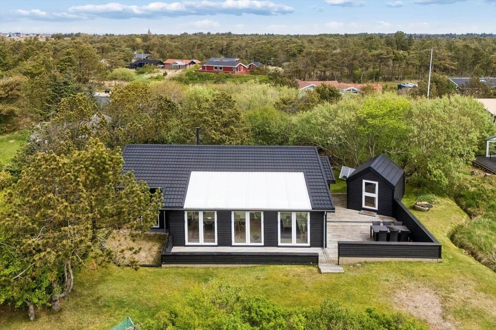 Schwarzes Ferienhaus mit Terrasse und Garten. Umgeben von Bäumen und Wald.