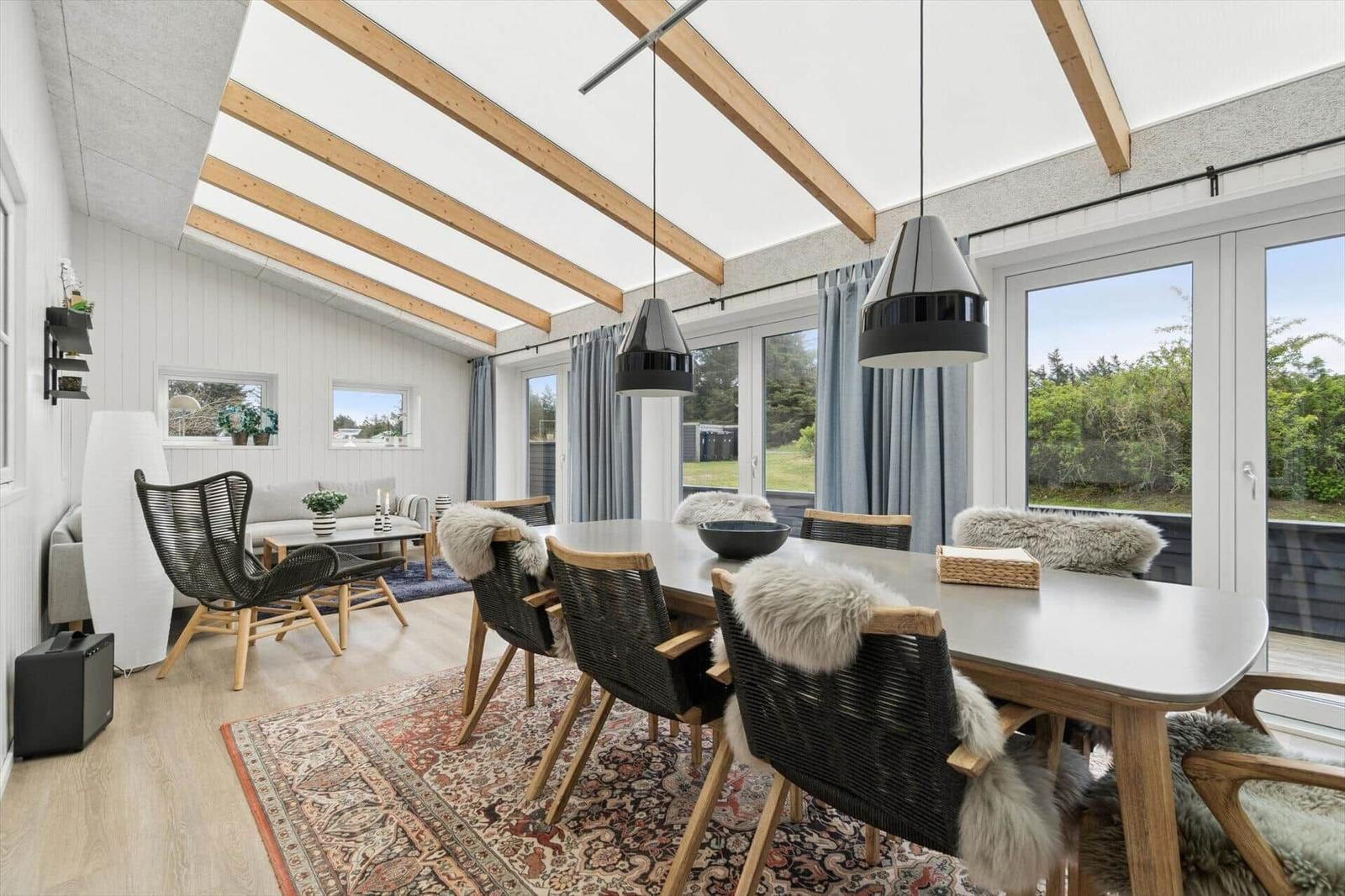 Essbereich mit Tisch, Stühlen und Fenstern. Decke mit Holzbalken und Hängelampen.