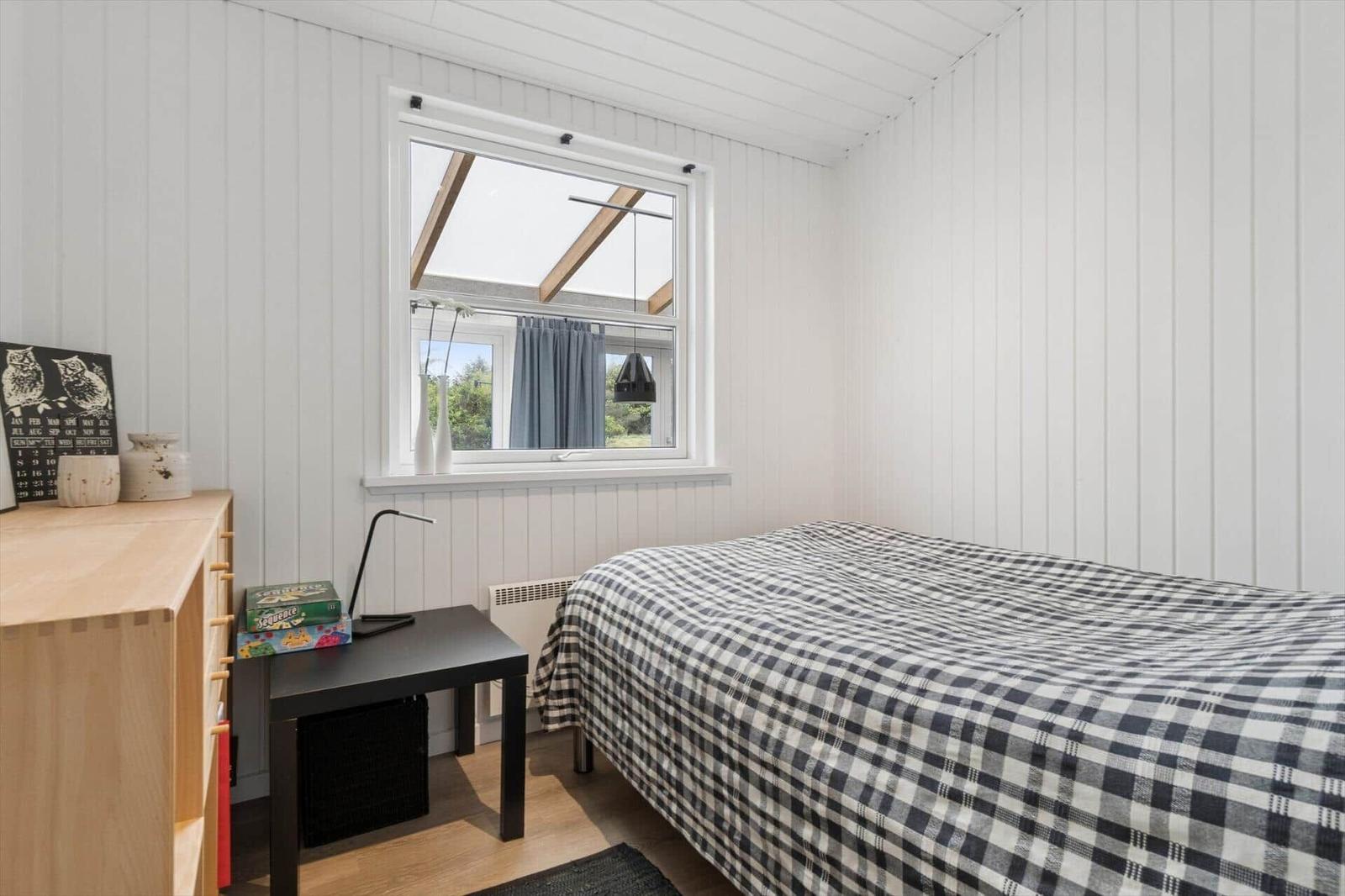 Schlafzimmer mit Bett, Schreibtisch und Fenster mit Blick nach draußen.