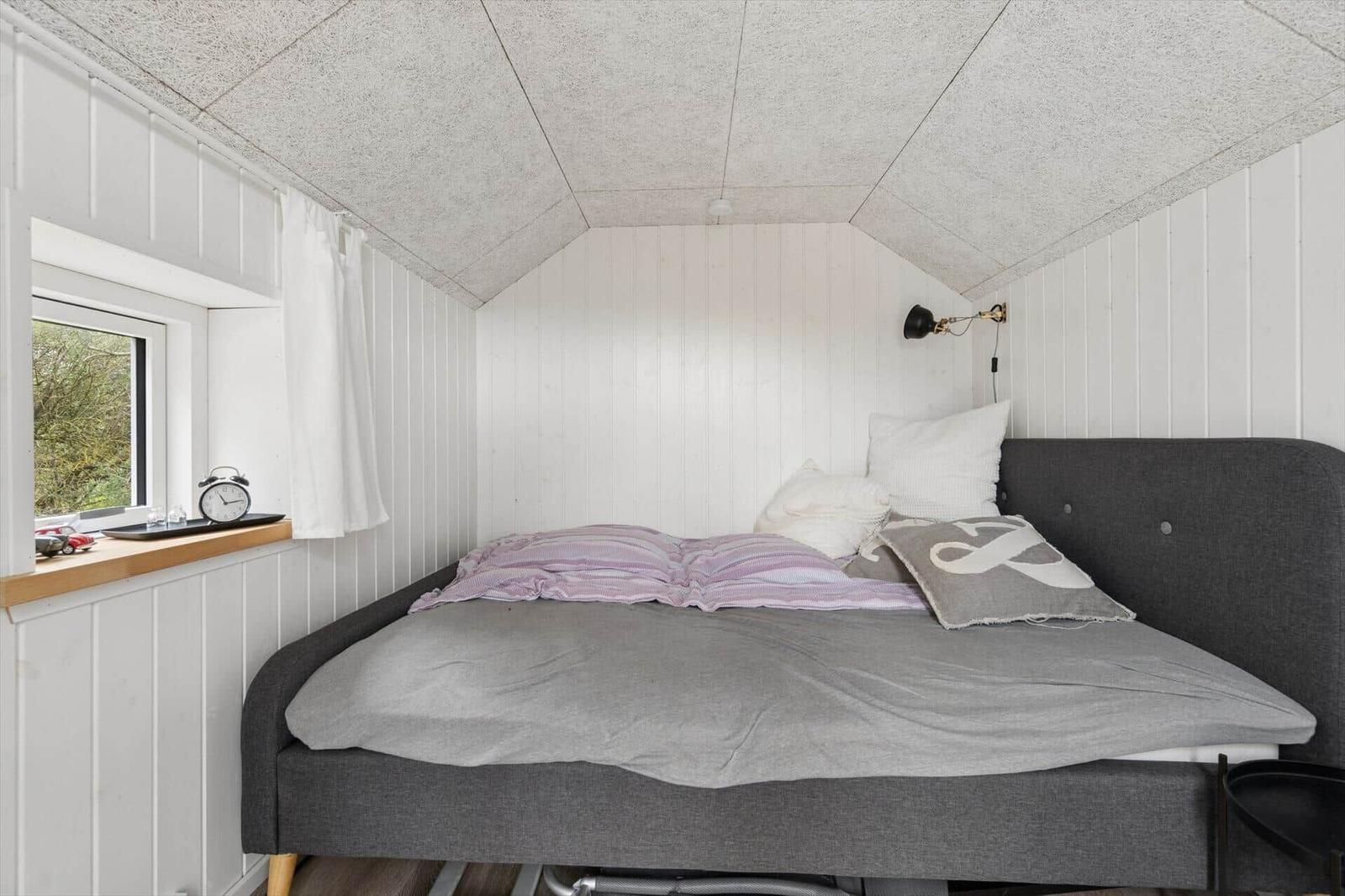 Schlafzimmer mit Bett, Fenster und Wandlampe.