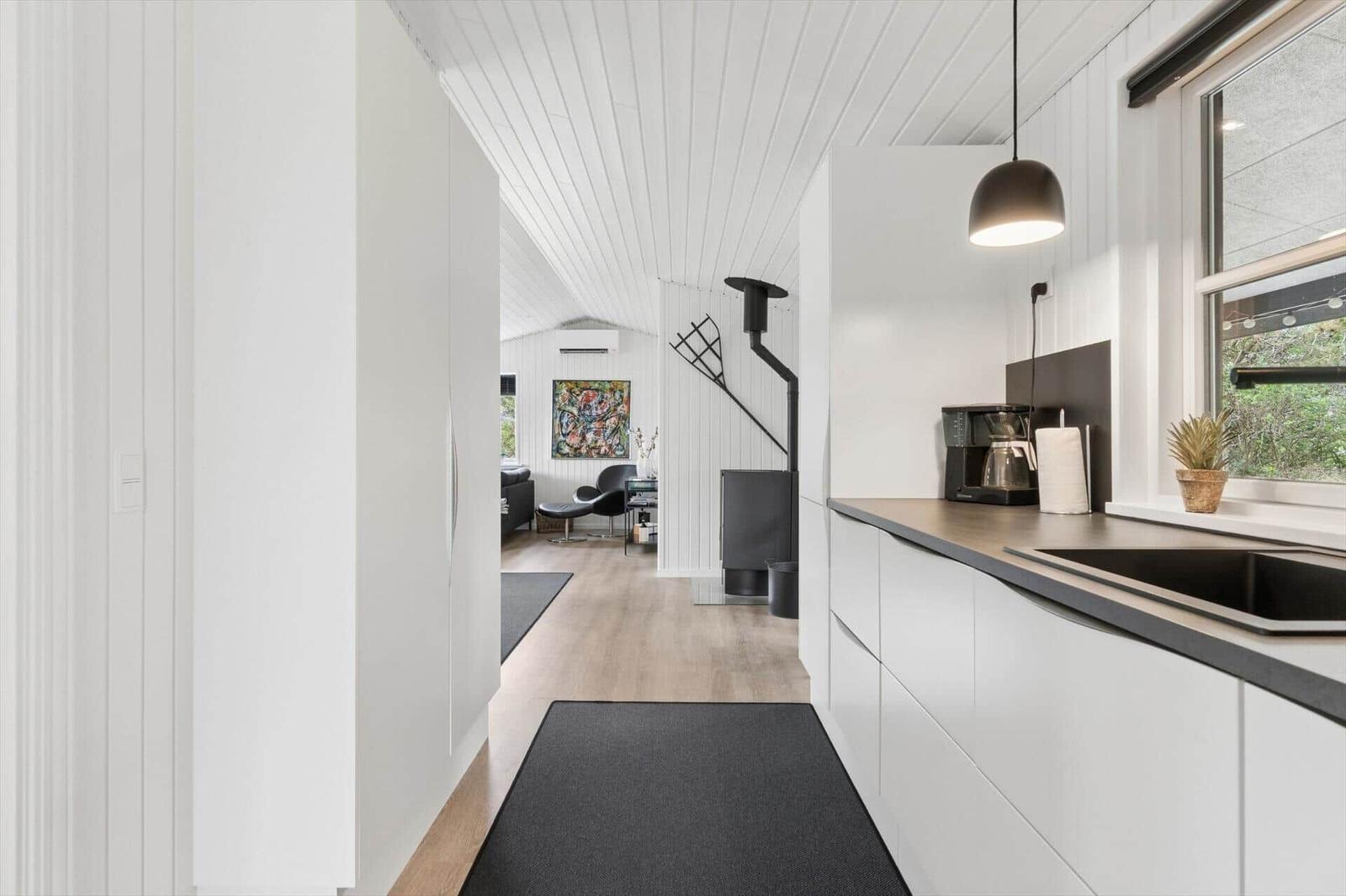 Küche mit Arbeitsplatte, Kaffeemaschine und Fenster. Blick in Wohnbereich mit Sofa und Kamin.