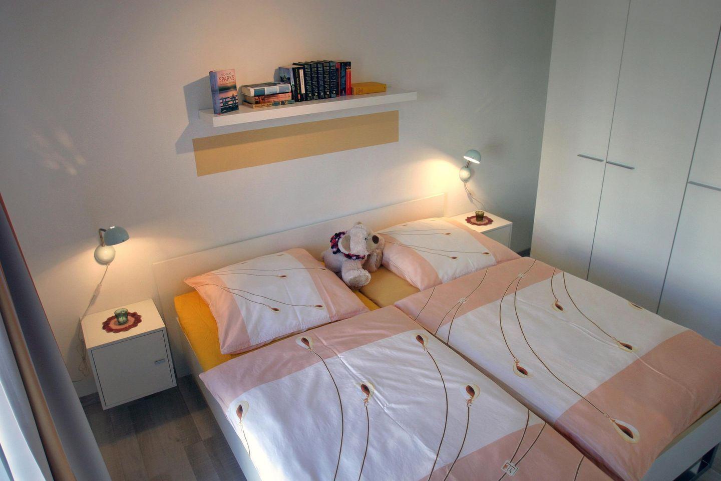 Schlafzimmer mit Doppelbett, Nachttischen und Bücherregal an der Wand.