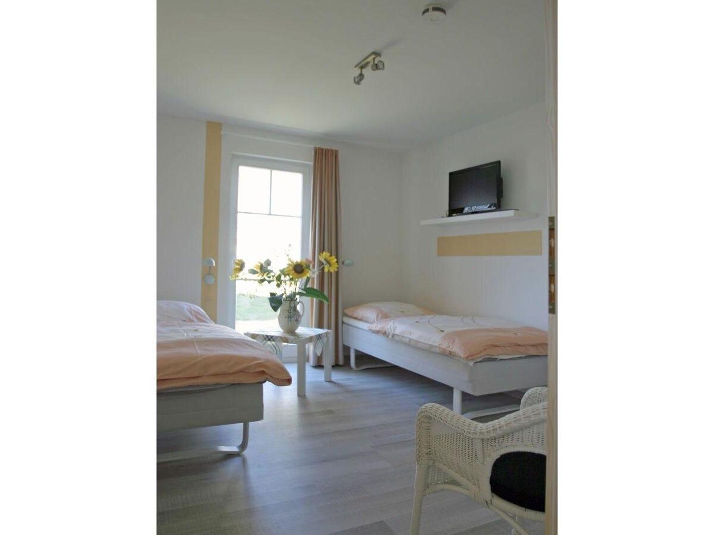 Zimmer mit zwei Betten, Fernseher und Fenster mit Sonnenblumen.