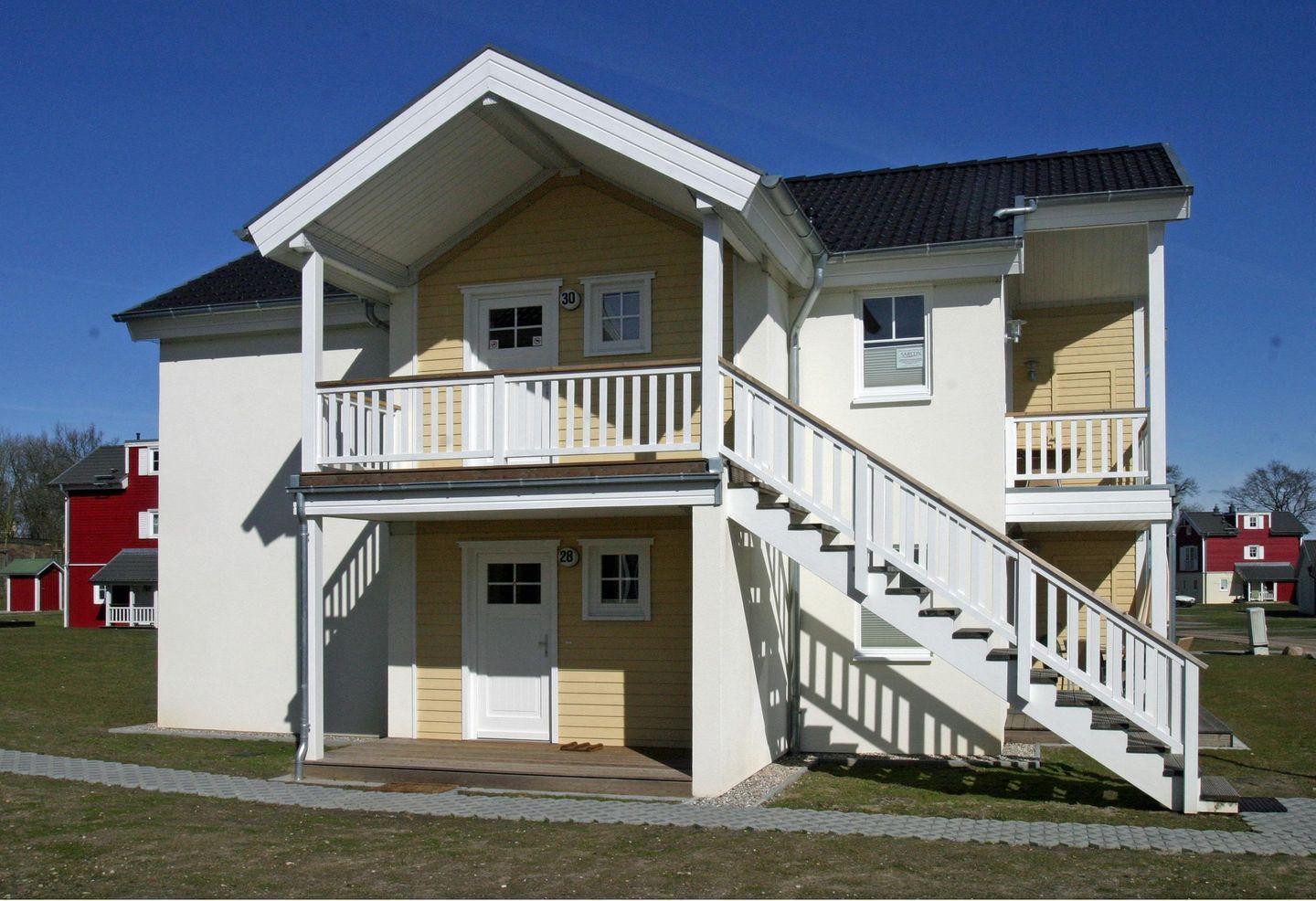 Zweistöckiges Ferienhaus mit weißen Balkonen und Treppe. Hausnummer 28 und 30.