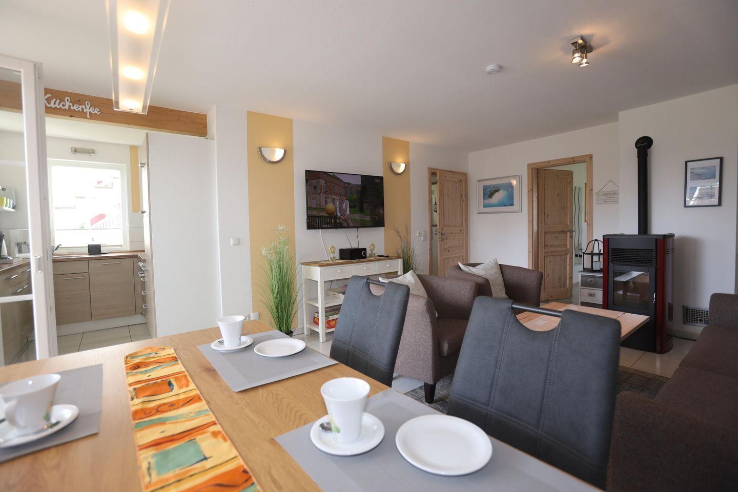 Essbereich mit Tisch und Stühlen. Im Hintergrund Küche und Wohnzimmer mit Kamin.
