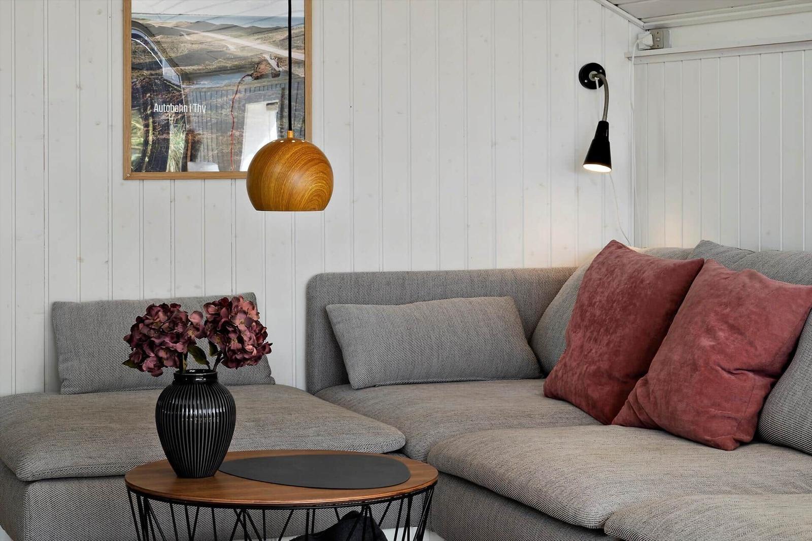 Ein grauer Sofa mit roten Kissen und einem runden Tisch mit Blumen.