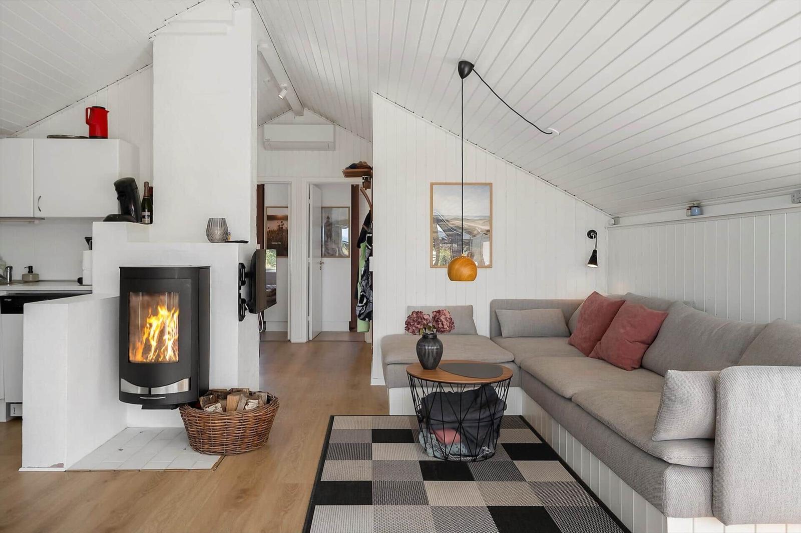 Wohnbereich mit Sofa, Kamin und Holzboden. Weiße Wände und schräger Deckenverlauf.