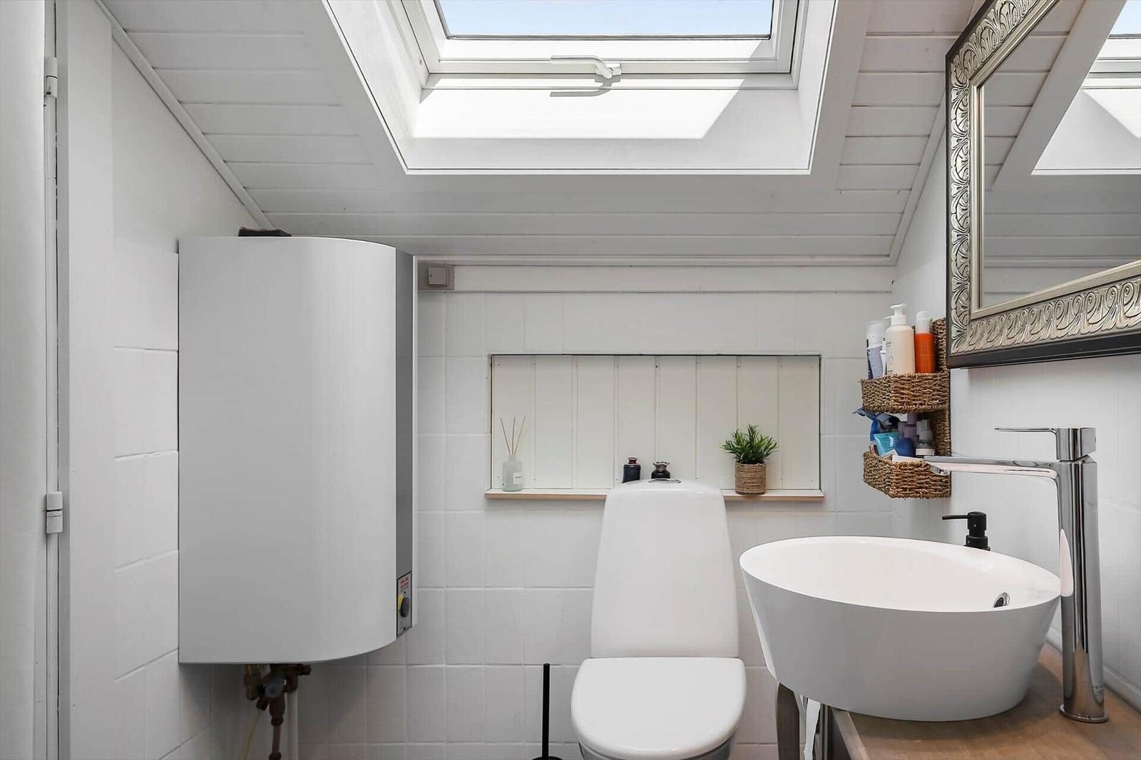 Badezimmer mit Dusche, Waschbecken und Toilette unter Dachfenster.