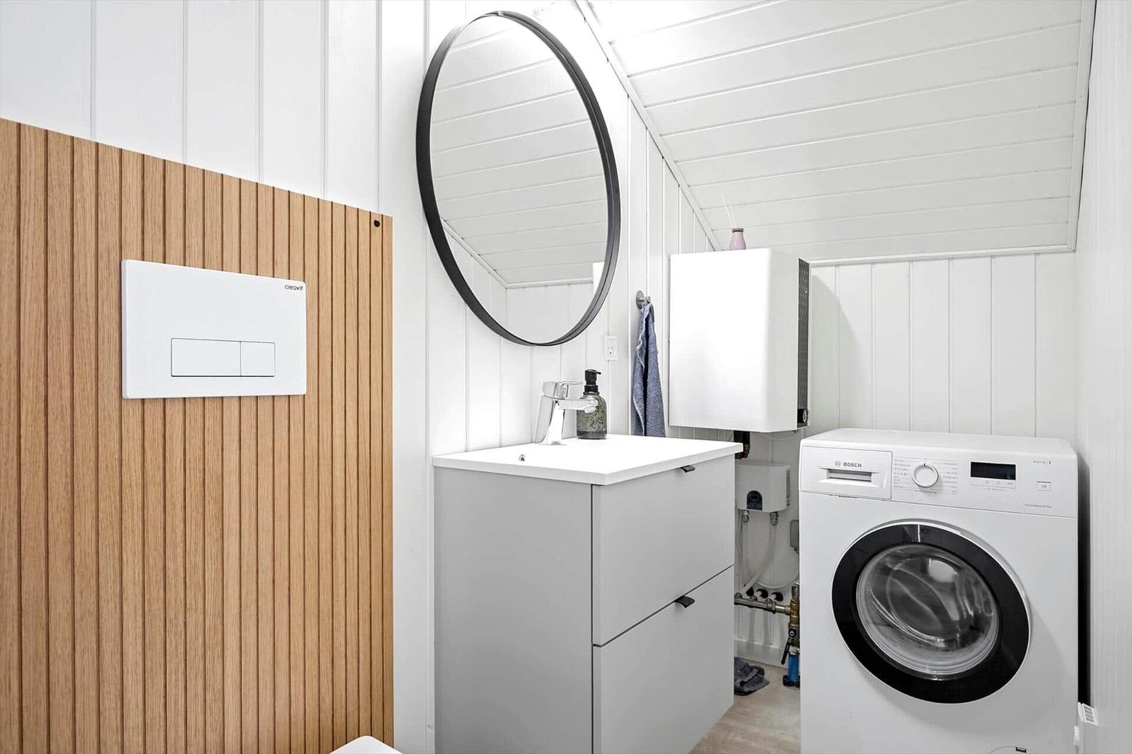Waschmaschine, Waschbecken und Spiegel in einem Raum mit Holzwand und weißen Paneelen.