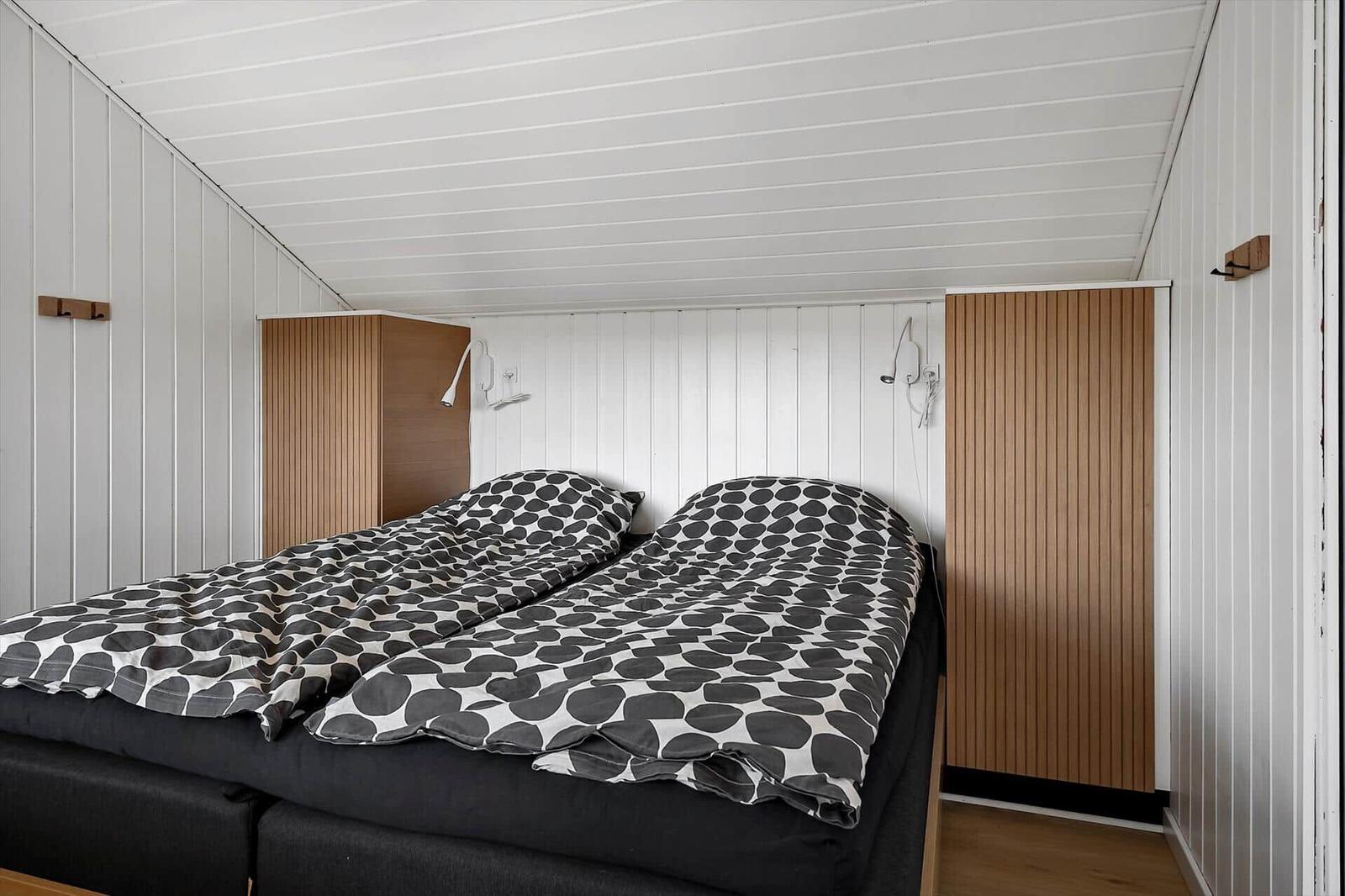 Schlafzimmer mit Doppelbett, weißen Wänden und Holzpaneelen an den Seiten.