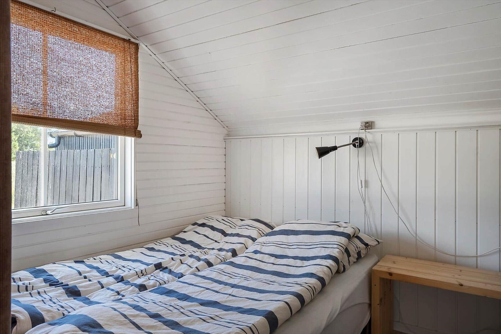 Schlafzimmer mit Doppelbett, Fenster und Wandlampe.