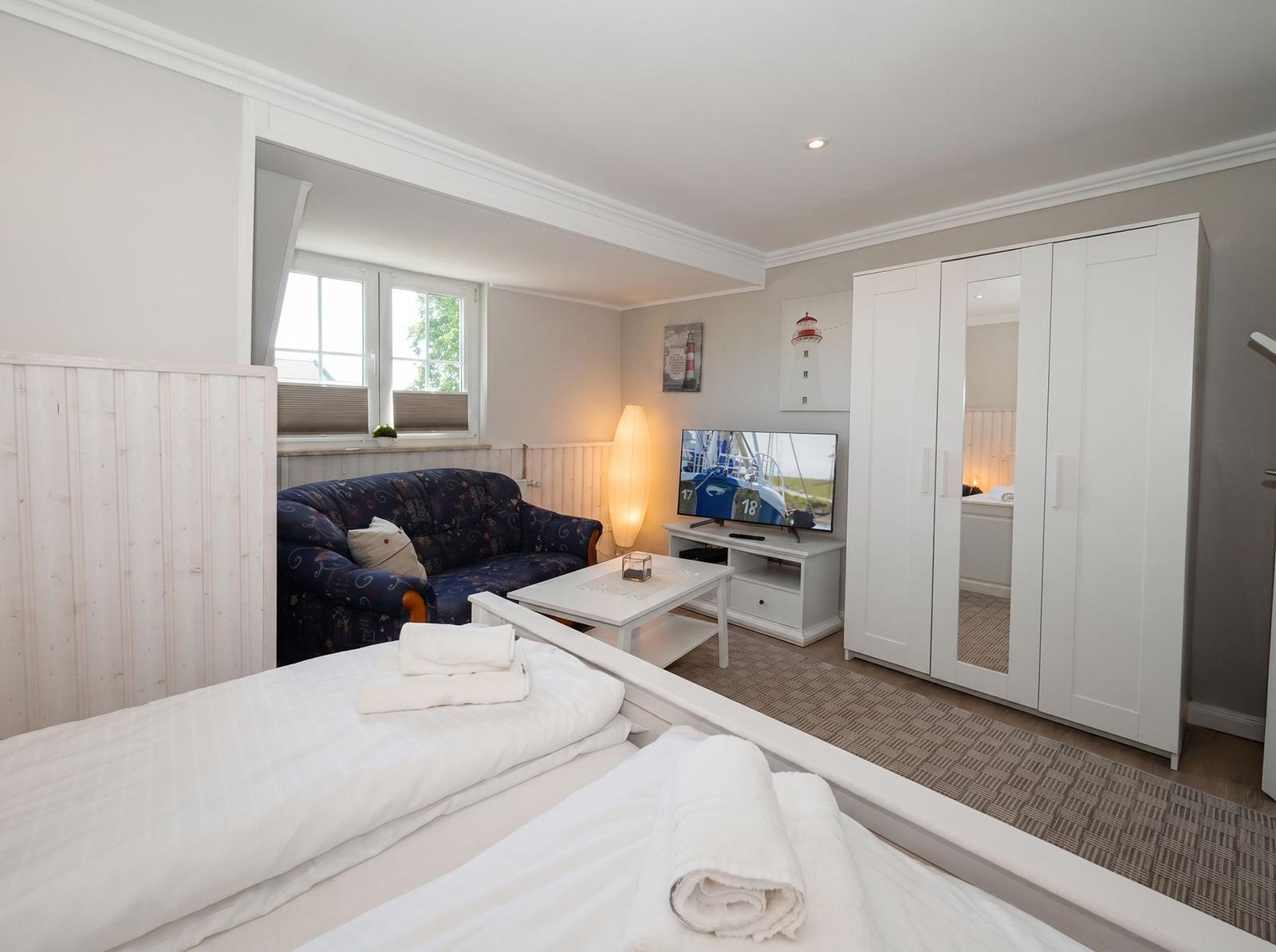 Zwei Betten mit Handtüchern, Sofa, Fernseher und Kleiderschrank im Zimmer.