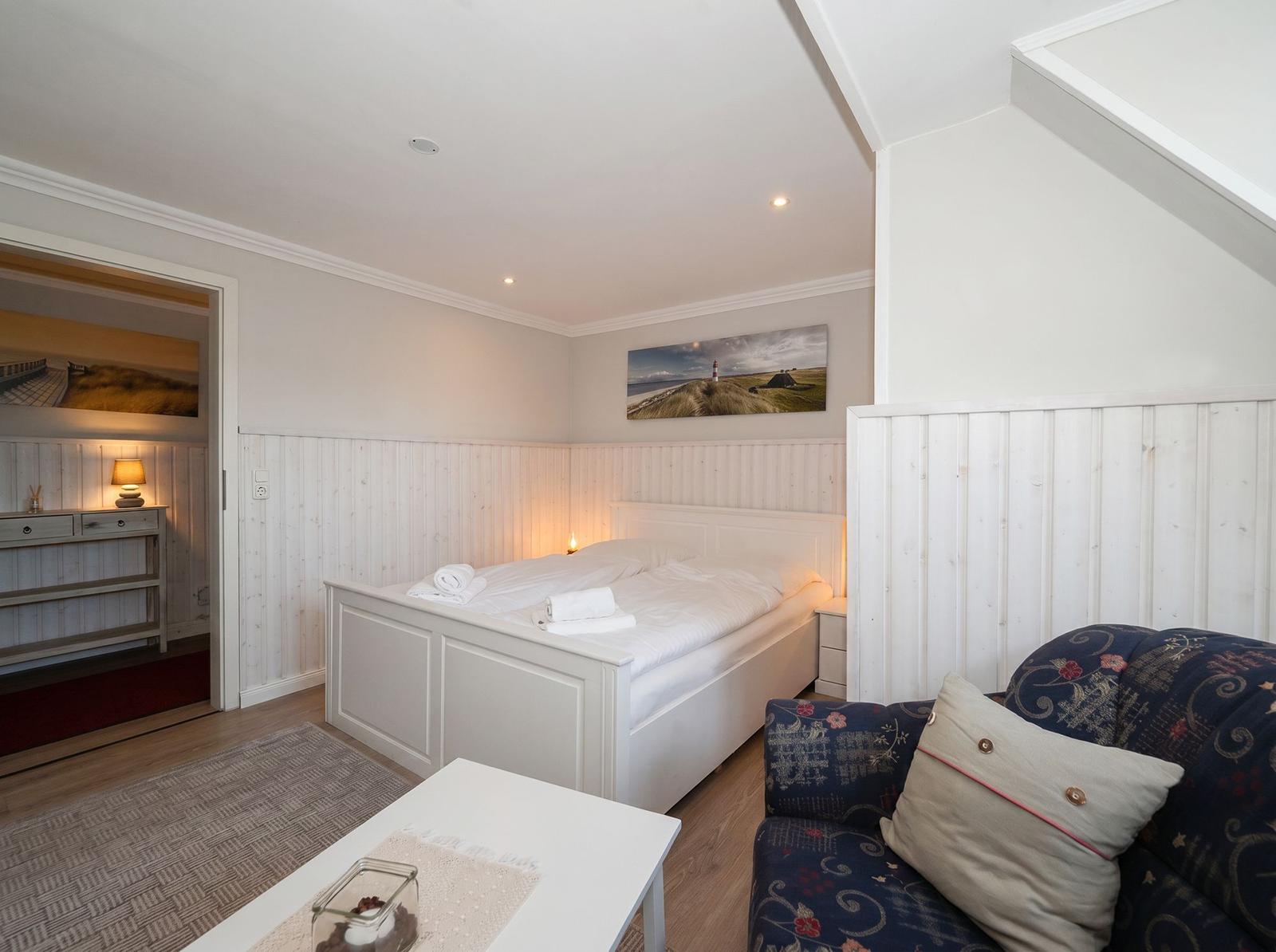 Schlafzimmer mit Bett, Sofa und Wandbild. Holzwand und Tür sichtbar.