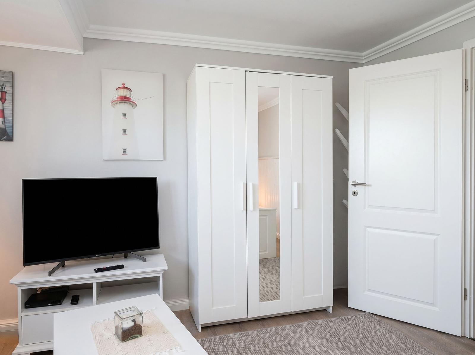 Schlafzimmer mit weißem Kleiderschrank, Fernseher und Lighthouse-Bild an der Wand.