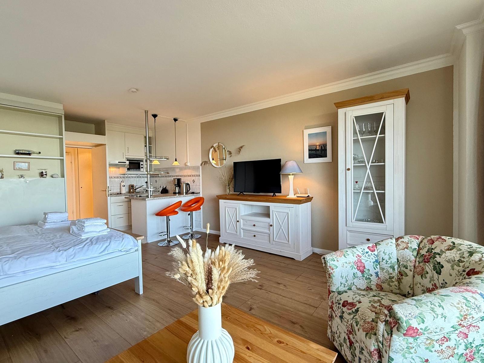 Apartment with bedroom, kitchen, and living area with TV and floral sofa.