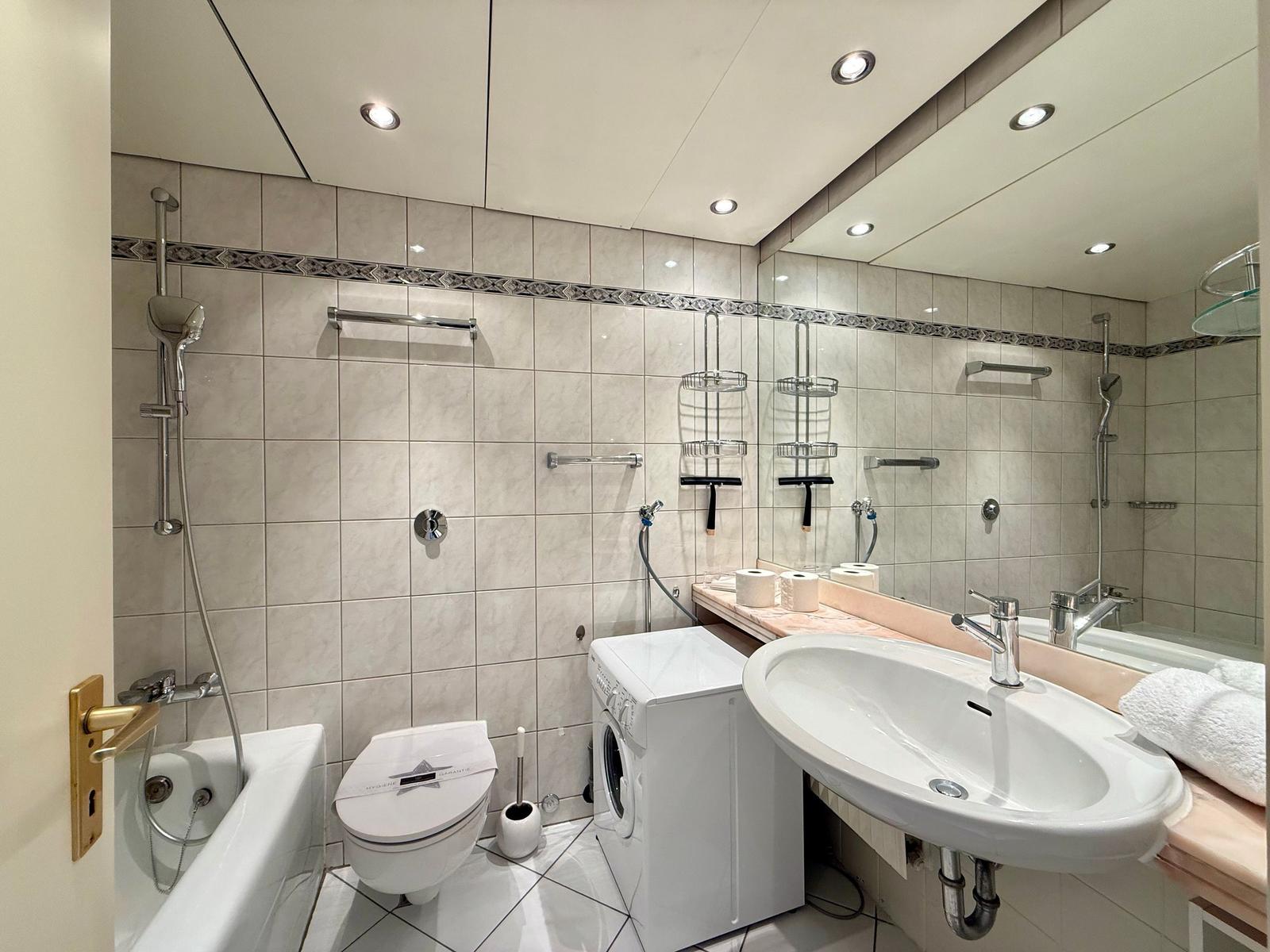 Bathroom with shower, toilet, washing machine, and sink.