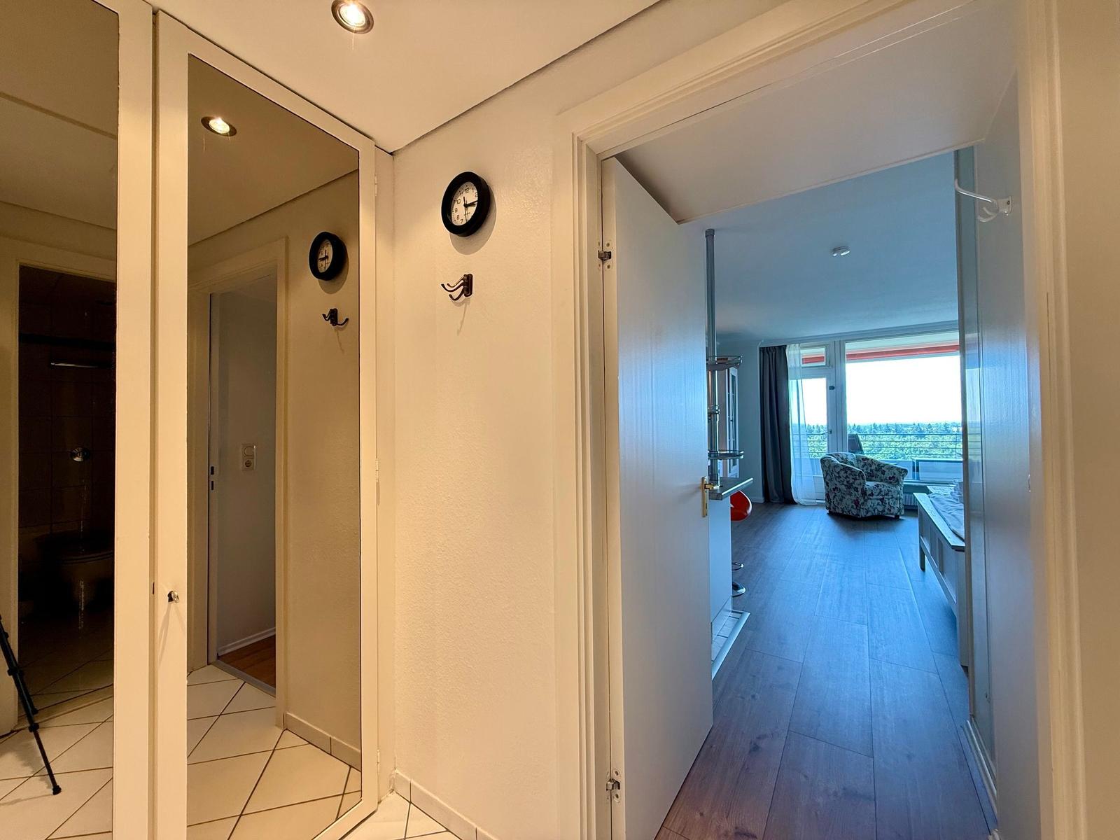 Hallway with view into bedroom and bathroom. Wall clock and hooks visible.