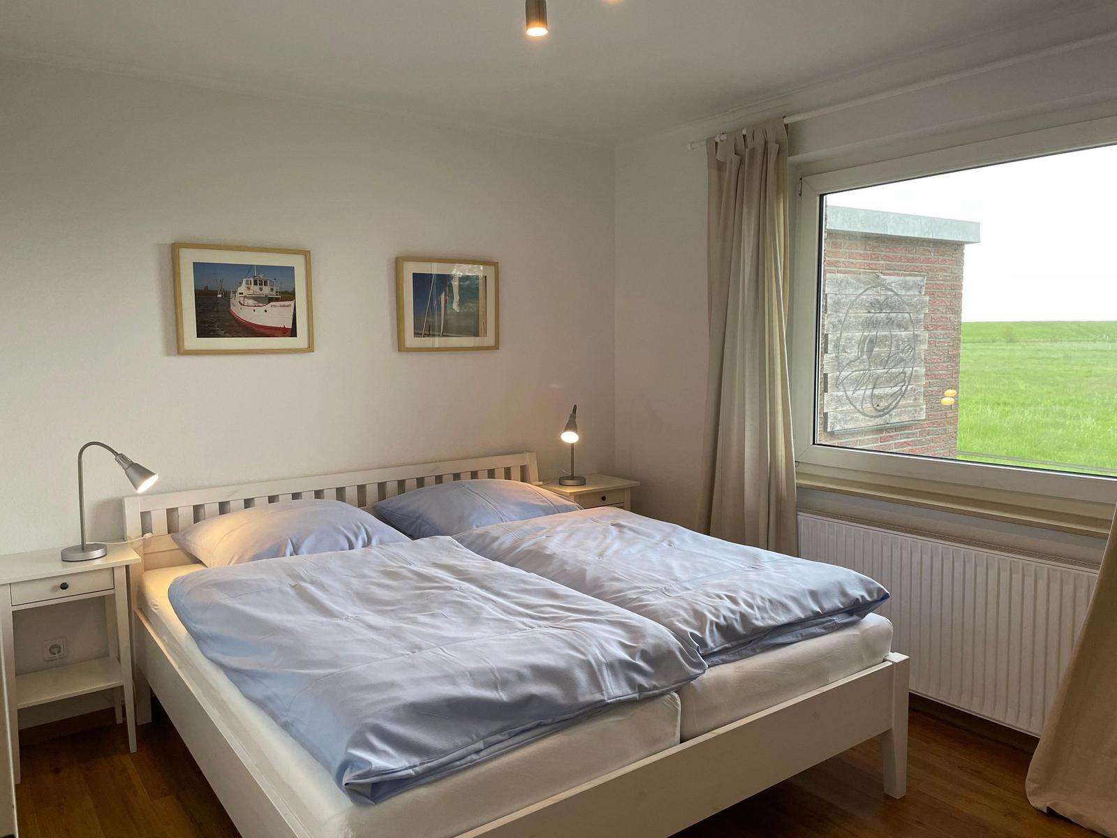 Schlafzimmer mit Doppelbett, zwei Nachttischen und Fensterblick auf Grünfläche.