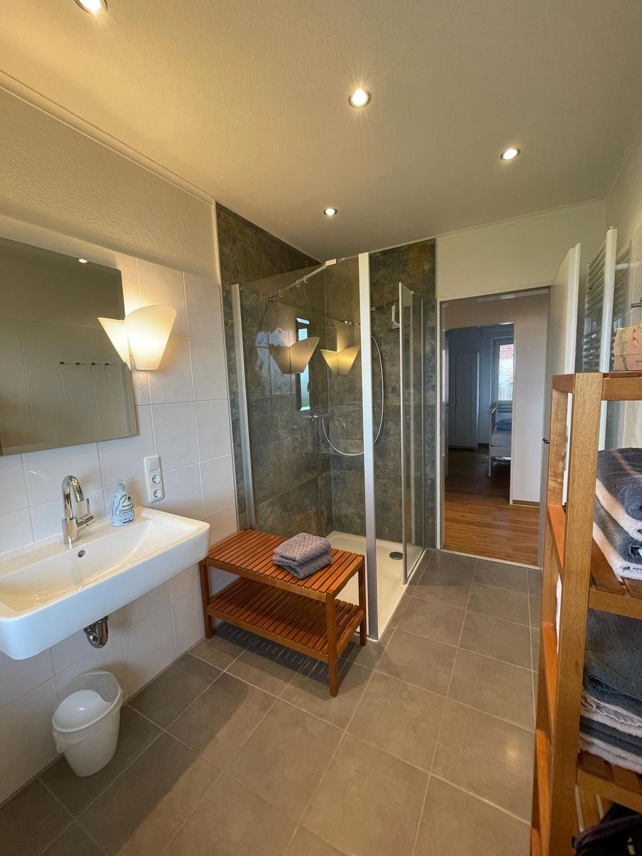 Badezimmer mit Dusche, Waschbecken und Holzbank.