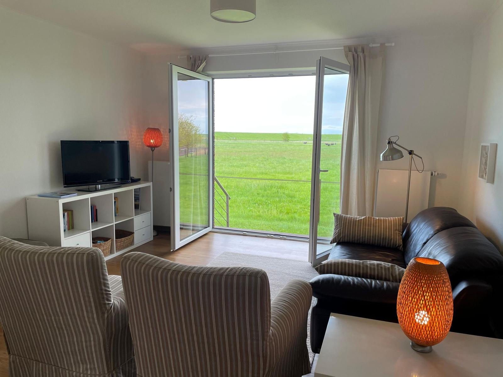 Wohnzimmer mit Sofa, Fernseher und Blick auf grünes Feld