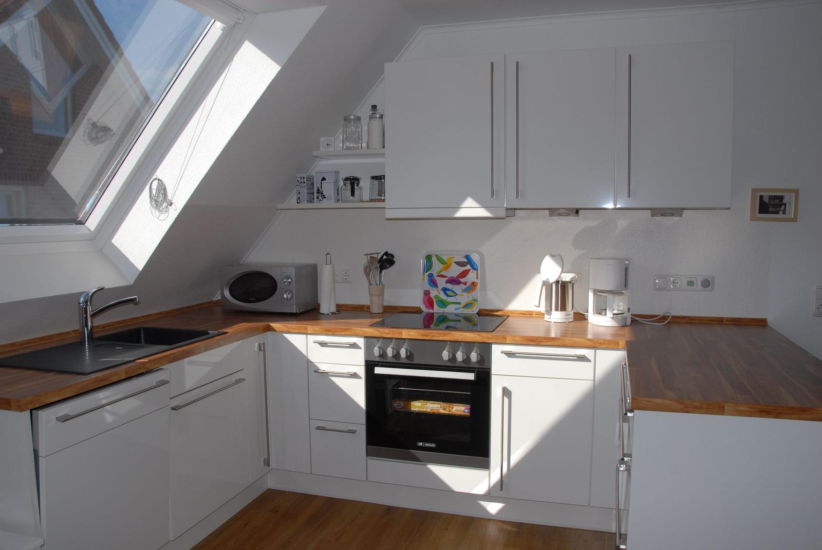 Küche mit weißen Schränken, Holzoberflächen und Dachfenster. Küchengeräte und -utensilien sind vorhanden.