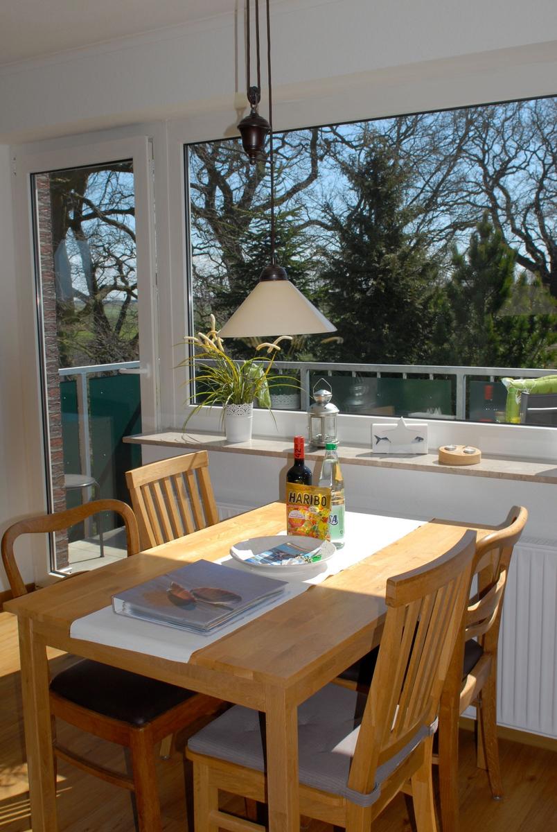 Esszimmer mit Holztisch, Stühlen und Blick auf Balkon mit Bäumen.