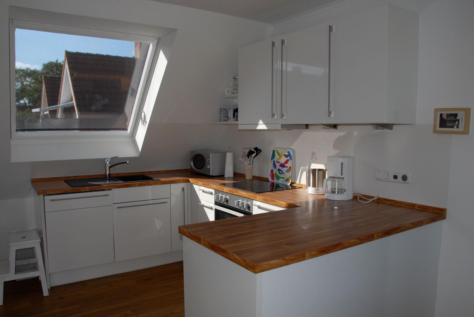 Küche mit Holzoberflächen, weißen Schränken und Fenster zum Blick nach draußen.