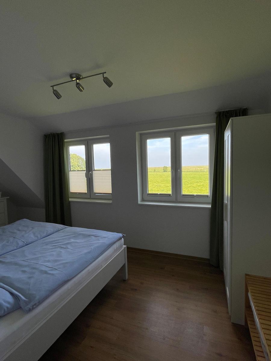 Schlafzimmer mit Doppelbett, Holzboden und Fenster zur grünen Landschaft.