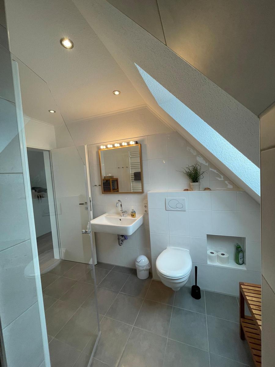 Badezimmer mit Dusche, Waschbecken und Toilette unter Dachschräge.