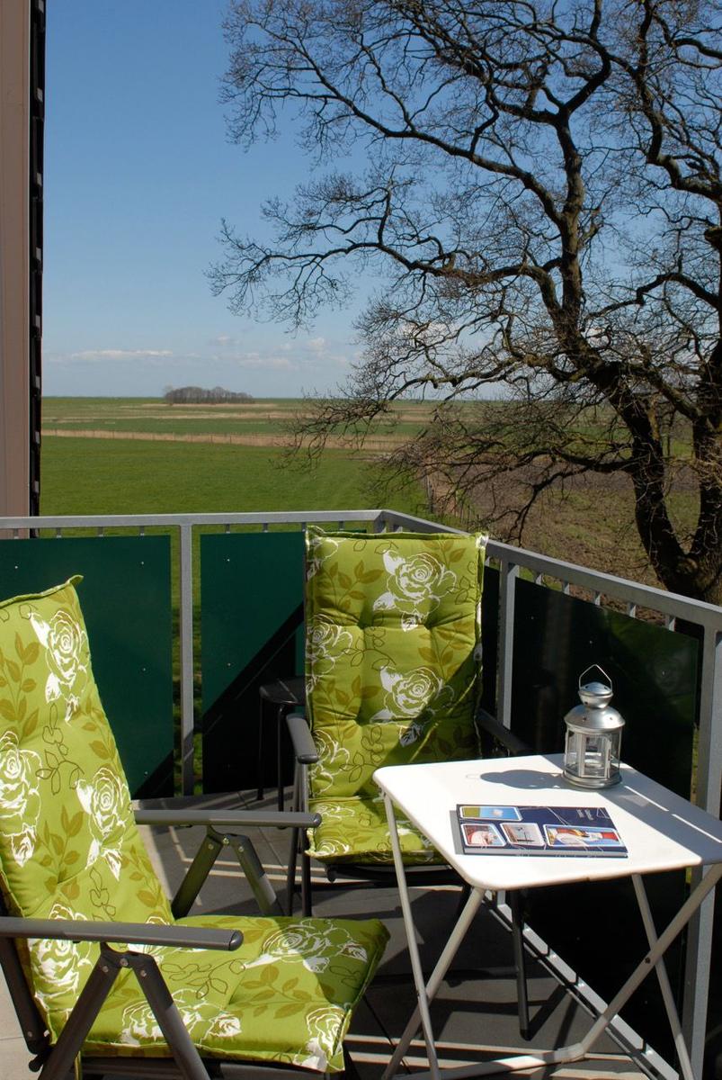 Balkon mit zwei grünen Stühlen und Tisch. Blick auf Feld und Baum.