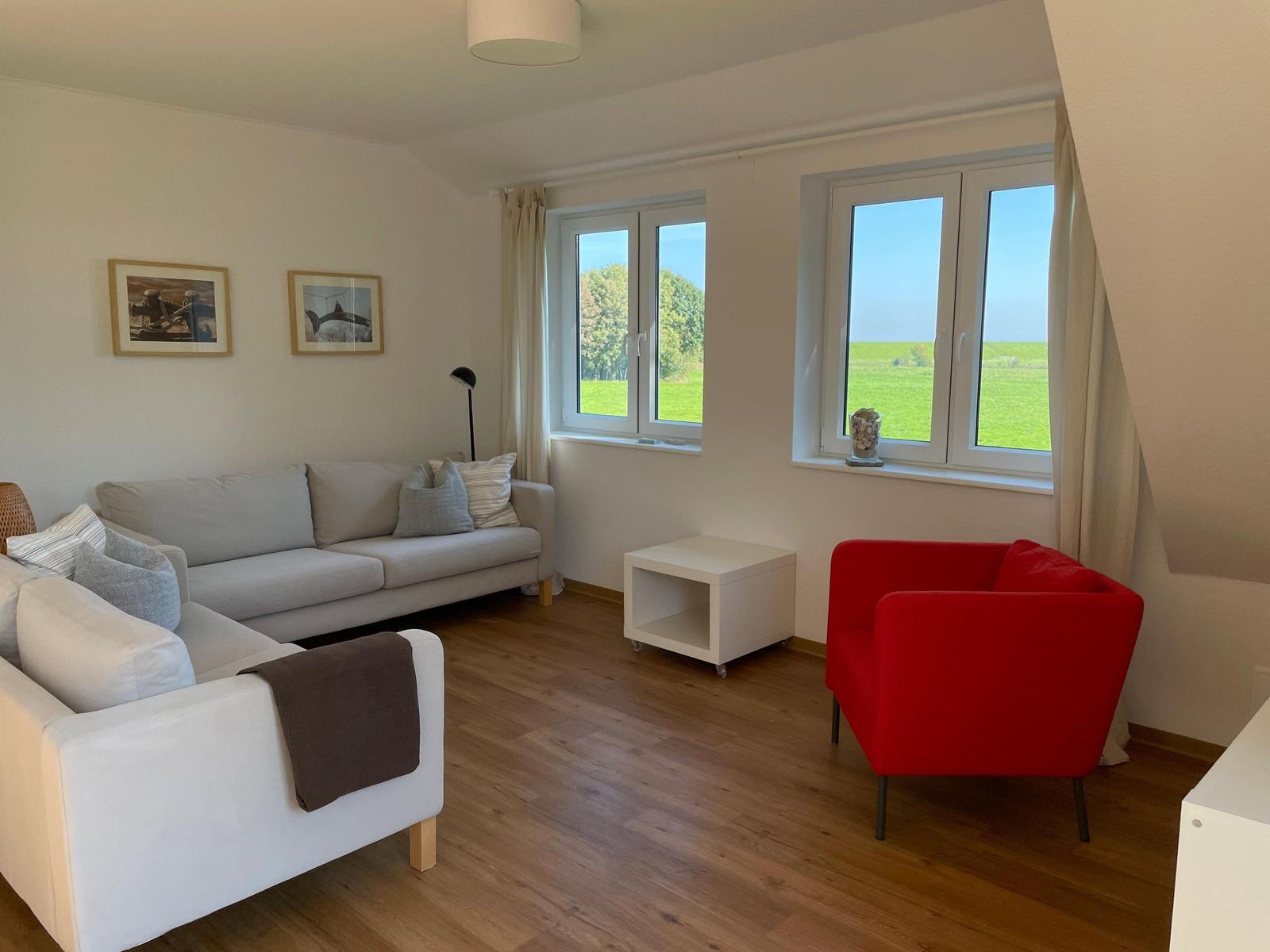 Wohnzimmer mit Sofa, rotem Sessel und Blick auf grünes Feld.