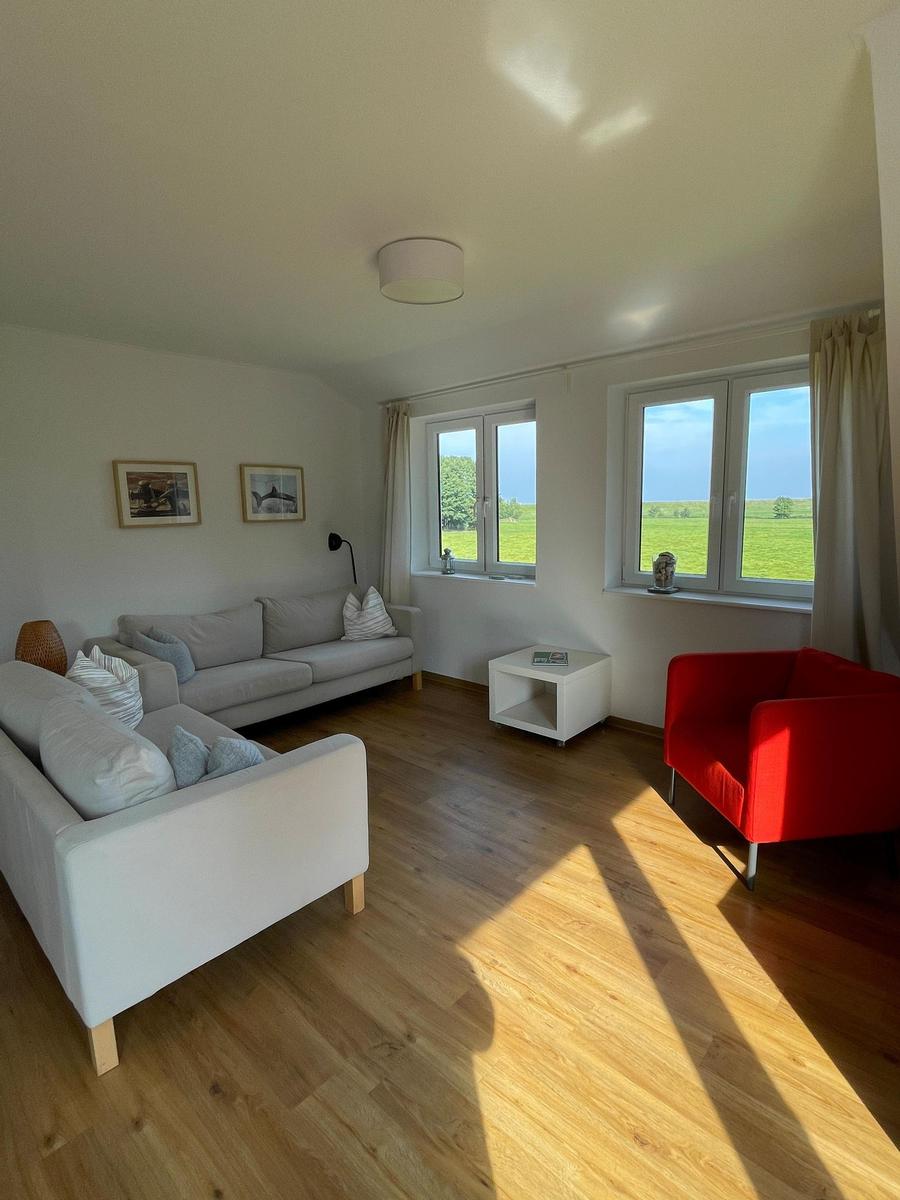 Wohnzimmer mit Sofa, rotem Sessel und Blick auf grünes Feld.
