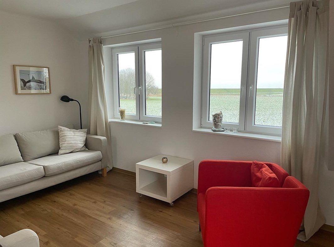 Wohnzimmer mit Sofa, rotem Sessel und Blick auf Felder
