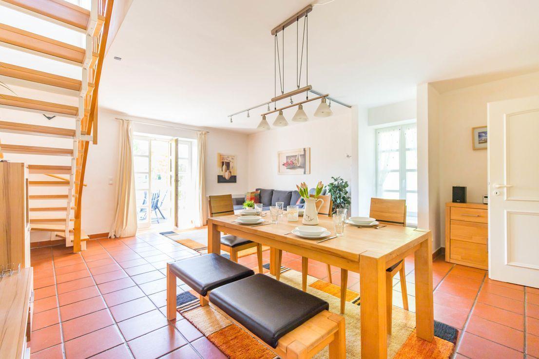 Esszimmer mit Holztisch, Stühlen und Treppenhaus. Terrassentür und Wohnbereich sichtbar.