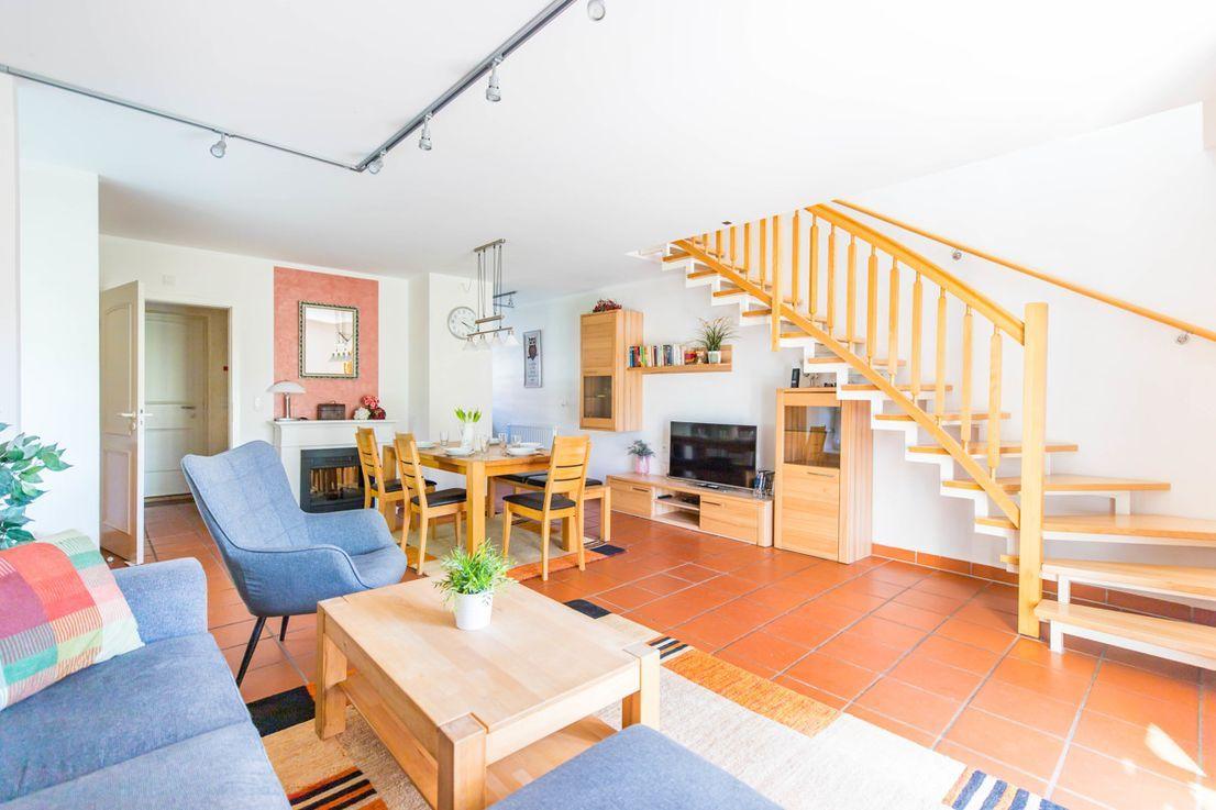 Wohnbereich mit Holztreppe, Sofa, Couchtisch und Esstisch.