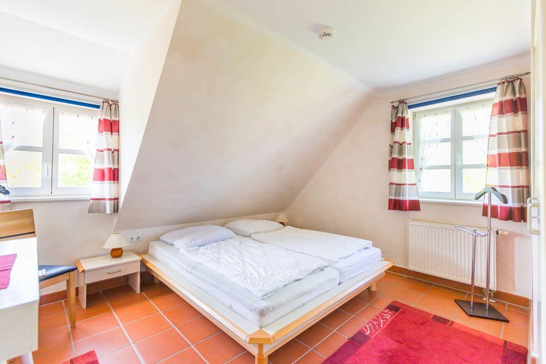 Schlafzimmer mit Doppelbett, zwei Fenstern und Holzboden.