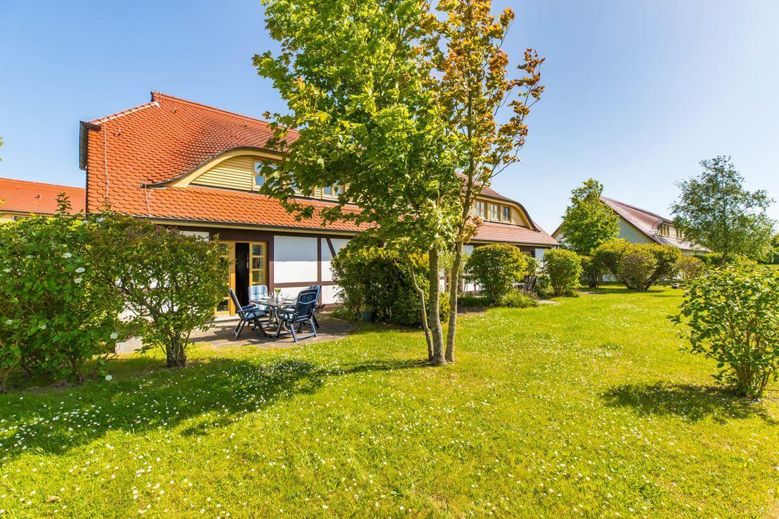 Haus mit Terrasse, Garten und Bäumen unter blauem Himmel.