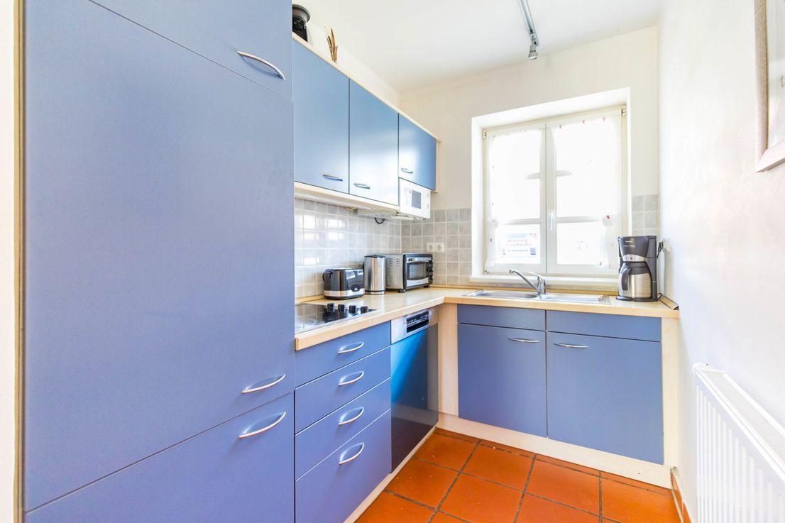 Küche mit blauen Schränken, Arbeitsplatte und Fenster.