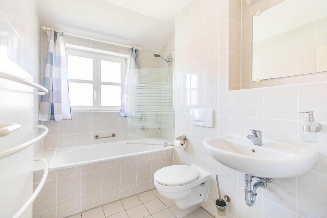 Badezimmer mit Badewanne, Dusche, Waschbecken und Toilette. Fenster mit Vorhängen.