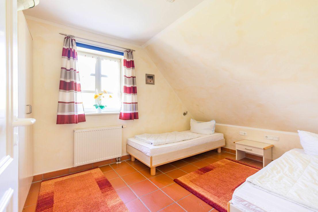 Zimmer mit zwei Betten, Fenster mit Vorhängen und Heizkörper an der Wand.