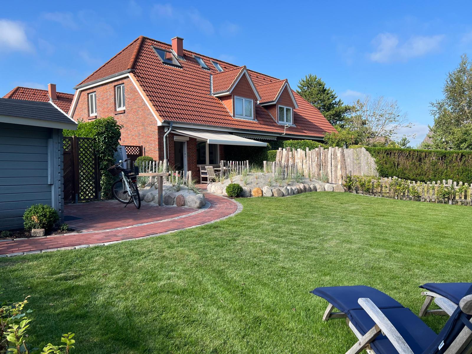 Haus mit rotem Dach, Garten mit Liegestühlen und Fahrrad.