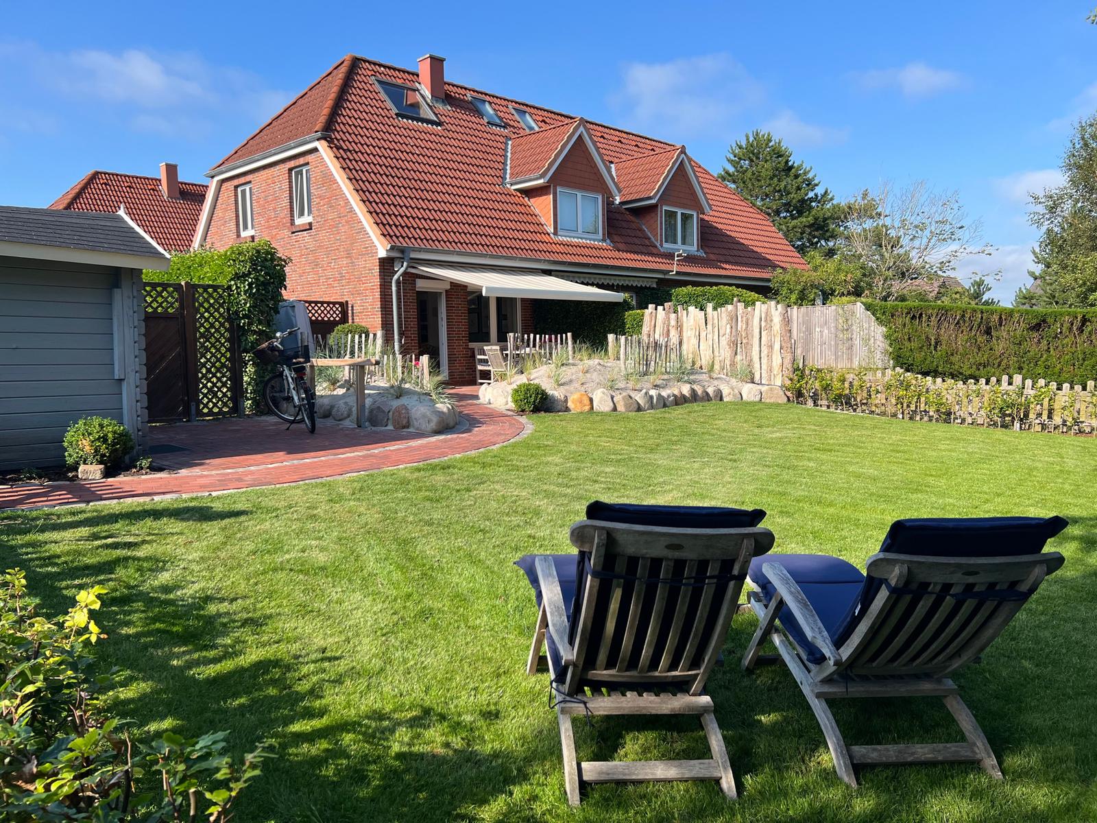 Haus mit Garten, zwei Liegestühle und Terrasse unter Sonnenschutz.
