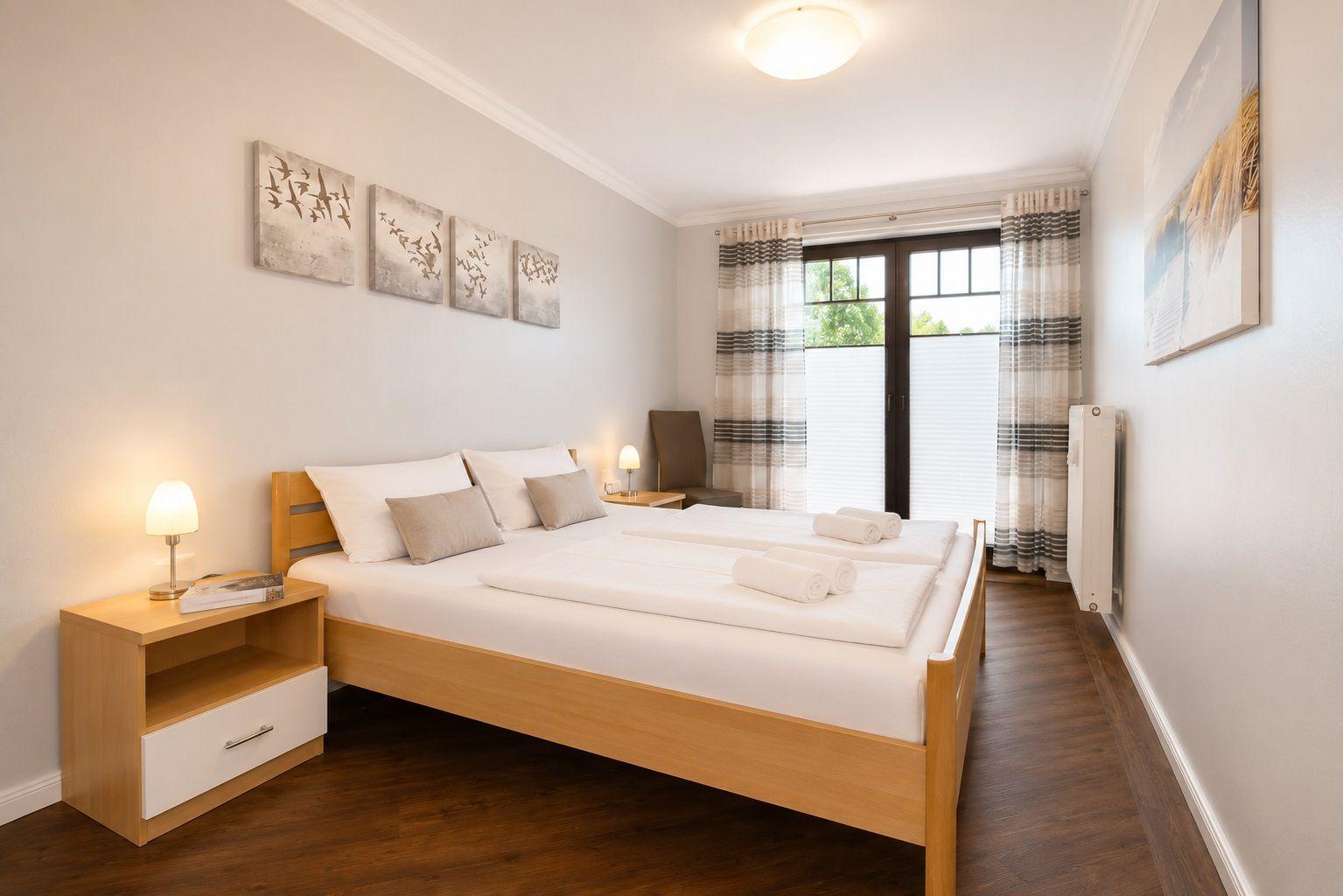 Schlafzimmer mit Doppelbett, Nachttisch, Fenster und Wandbildern.
