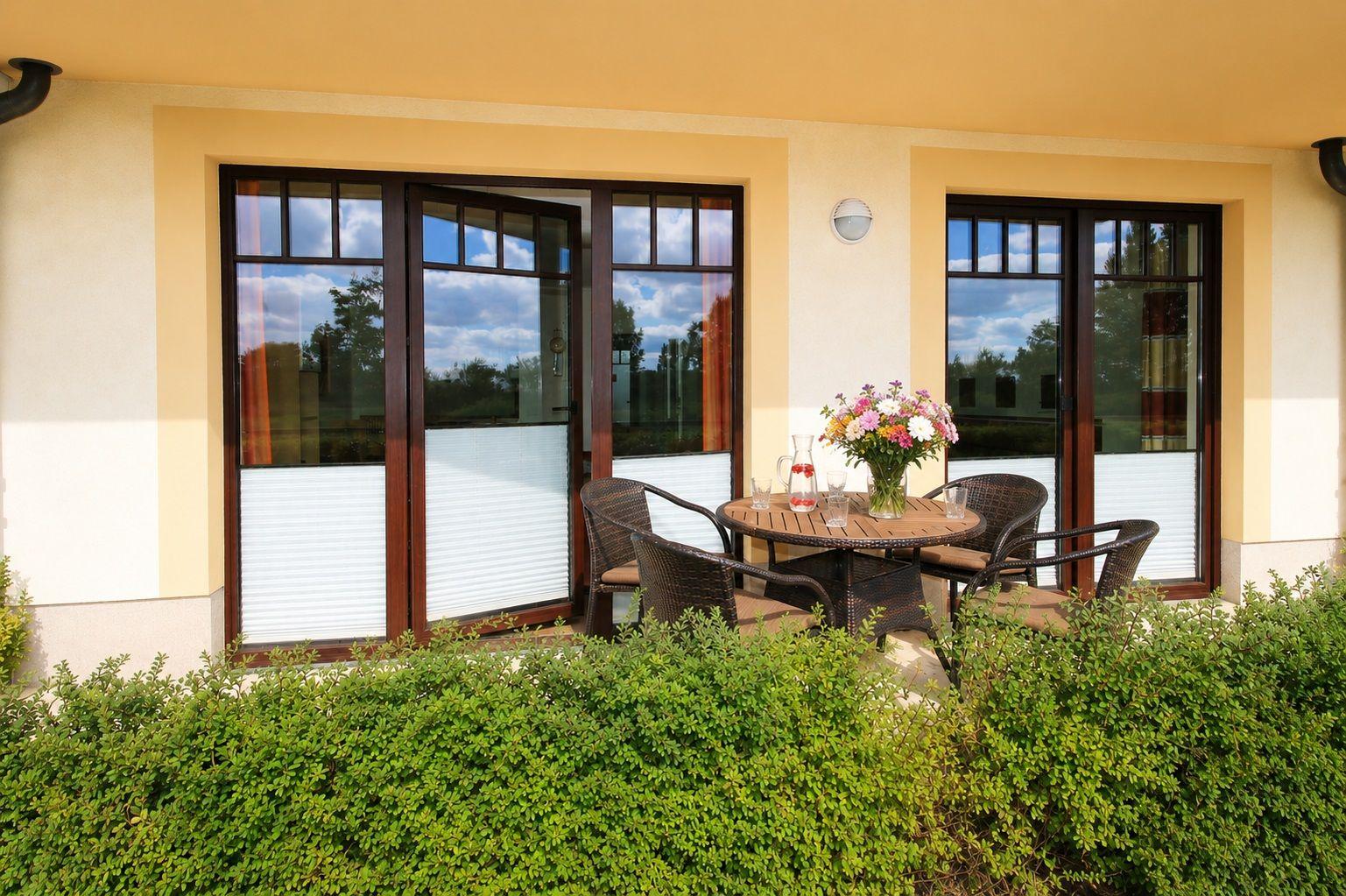 Terrasse mit Tisch, Stühlen und Blumen vor einem Haus mit Fenstern.