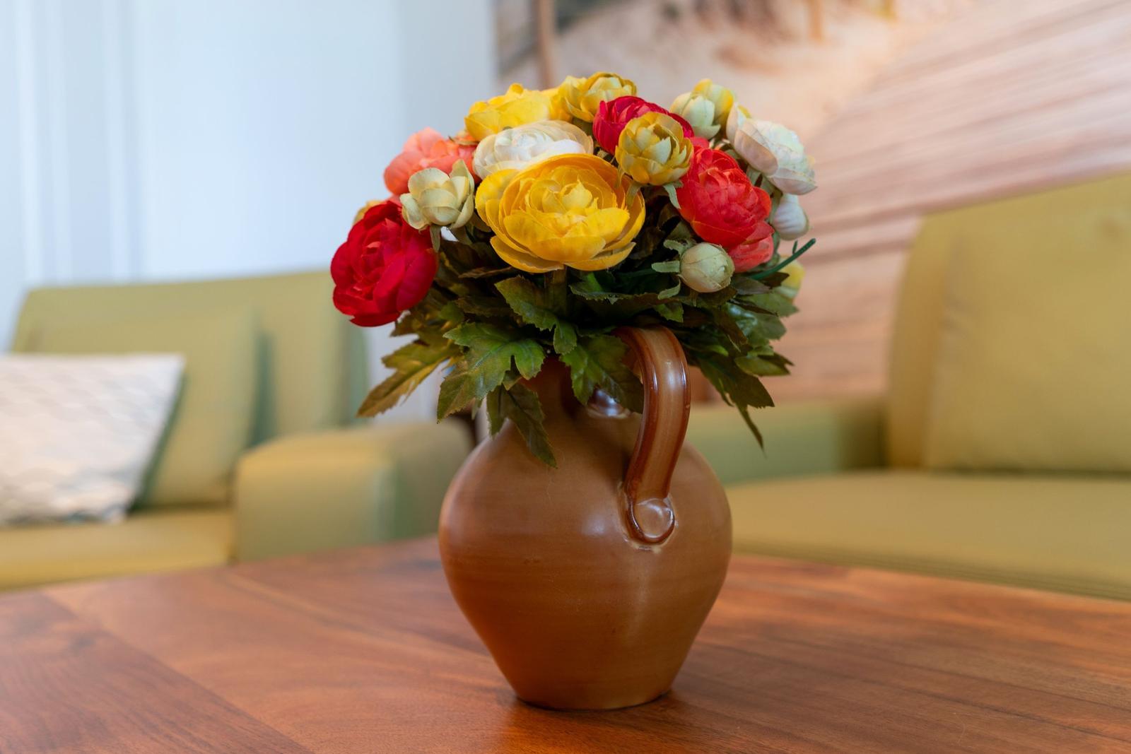 Flower bouquet in brown ceramic jug on wooden table in front of sofa