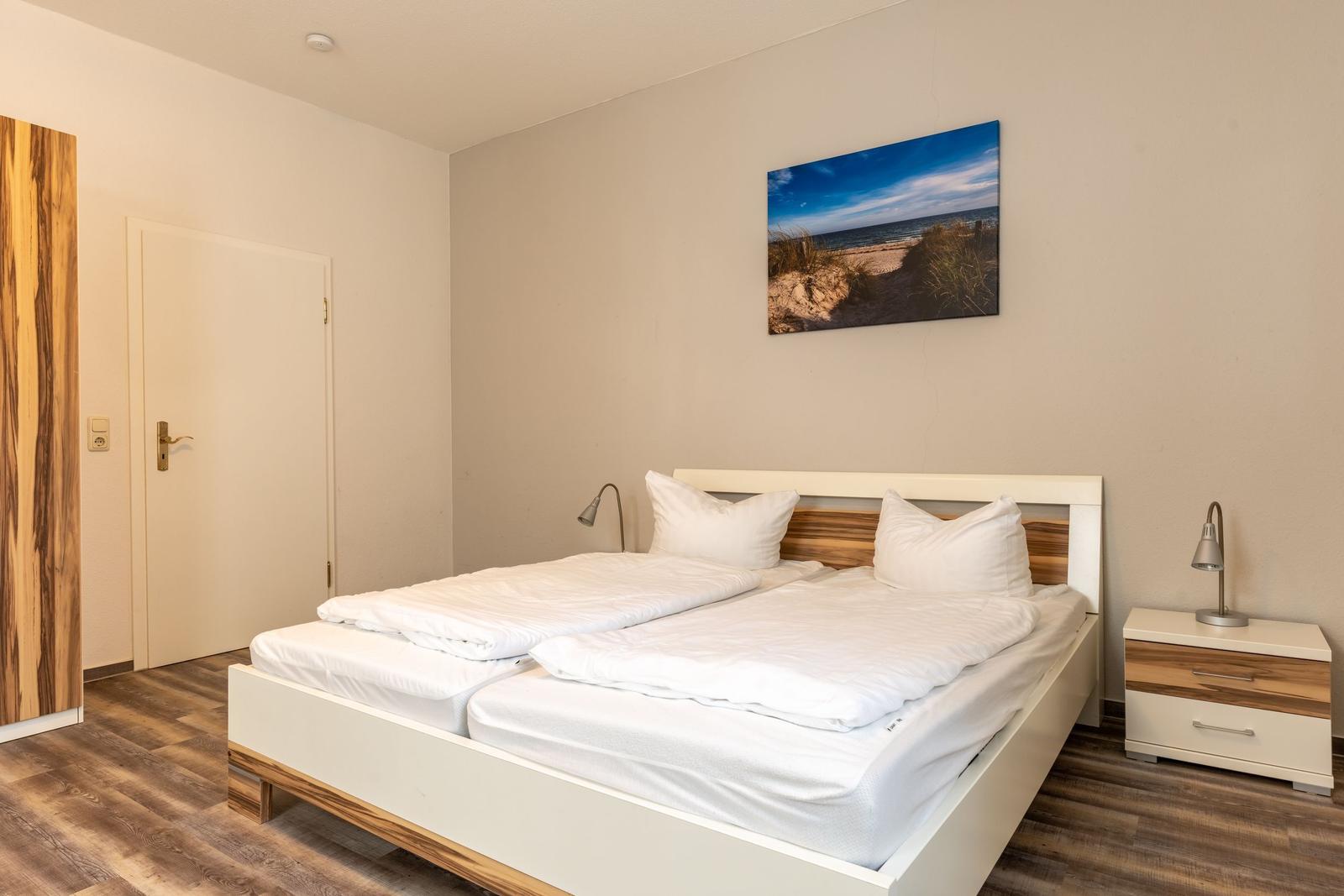Bedroom with double bed, nightstand, and wall art. Wooden floor and door visible.