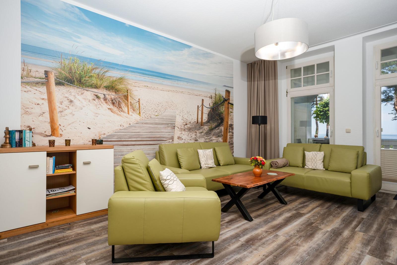 Living room with green sofas, wooden floor, and beach mural on the wall.